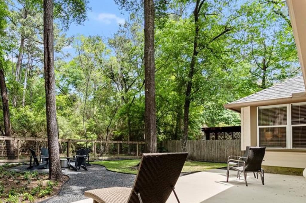 Serene backyard patio with outdoor seating, surrounded by lush green trees and a wooden fence, ideal for relaxing and outdoor entertaining.