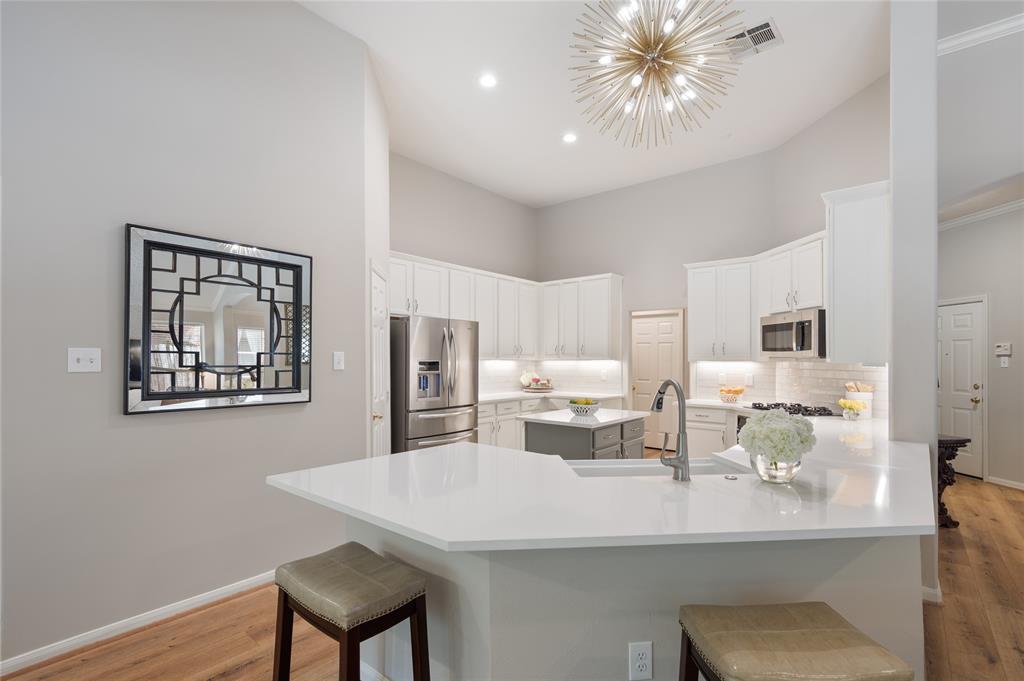 Bright modern kitchen with white cabinetry, stainless steel appliances, and a central island featuring a sleek sink and contemporary pendant lighting.