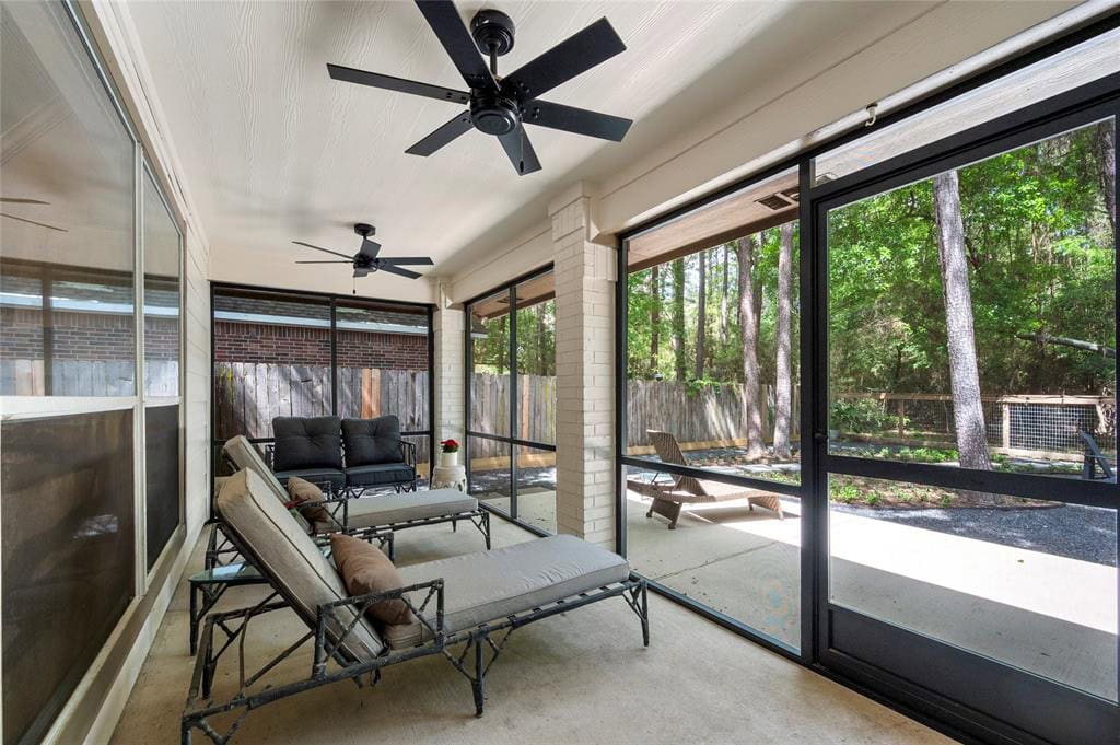 Bright screened-in porch with comfortable outdoor seating, ceiling fans, and views of lush greenery and mature trees, creating a relaxing indoor-outdoor living space.
