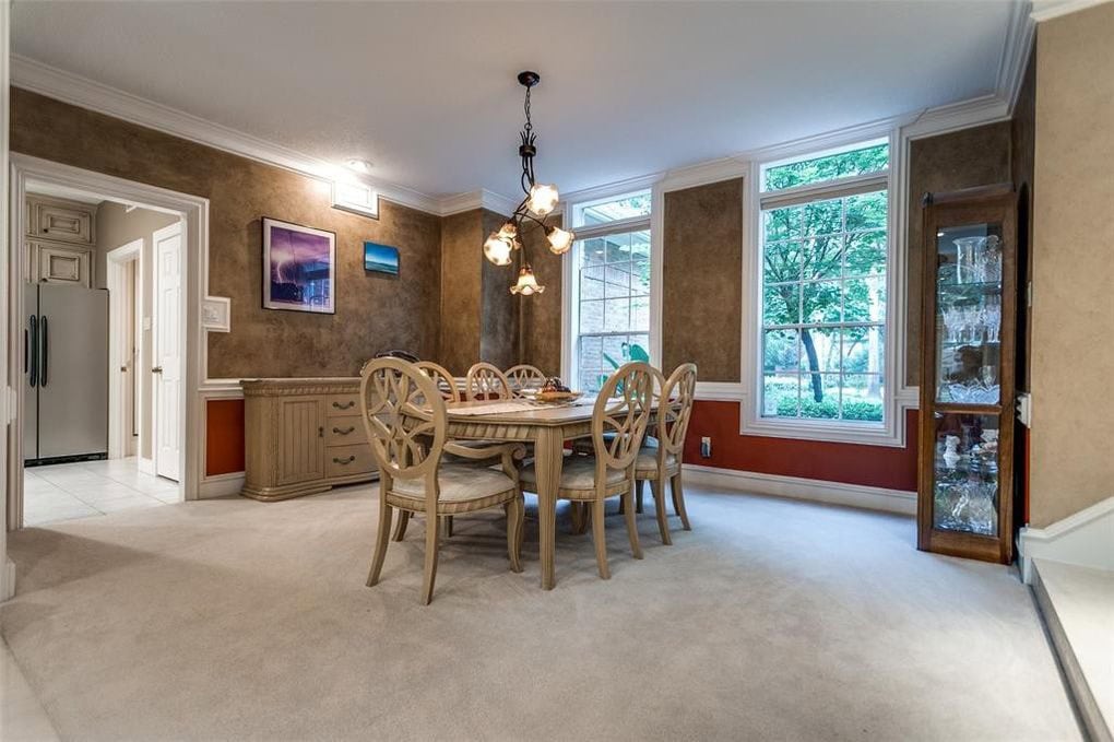 Elegant traditional dining room featuring a wooden dining table with six matching chairs, a classic chandelier, large windows with lush outdoor views, and a glass display cabinet, creating a warm and inviting interior.