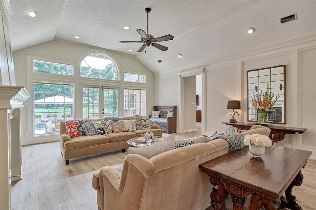 Spacious living room with large windows, vaulted ceiling, ceiling fan, and neutral-toned furniture, creating a bright, airy, and comfortable interior space.
