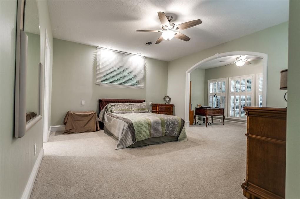 Luxurious master bedroom with a large bed, wooden furniture, ceiling fans, and an adjoining sitting area with bay windows, creating an elegant and spacious interior design.